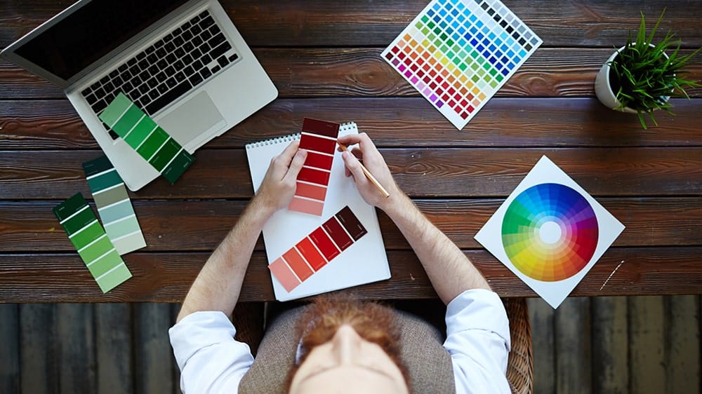 Diseñador gráfico frente a una mesa, contrastando diferentes paletas de colores pantones.