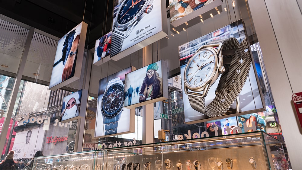 Interior de tienda de relojes con varias cajas de luz colgando de techo, con publicidad impresa con impresión digital