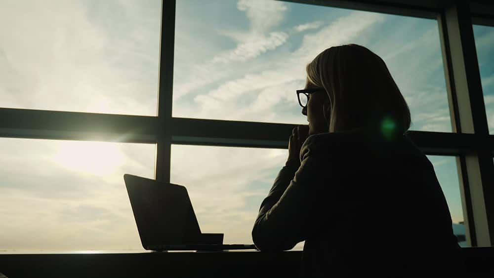 Mujer mirando un ordenador portátil junto a una ventana protegida con láminas de filtro solar para oficinas eficientes