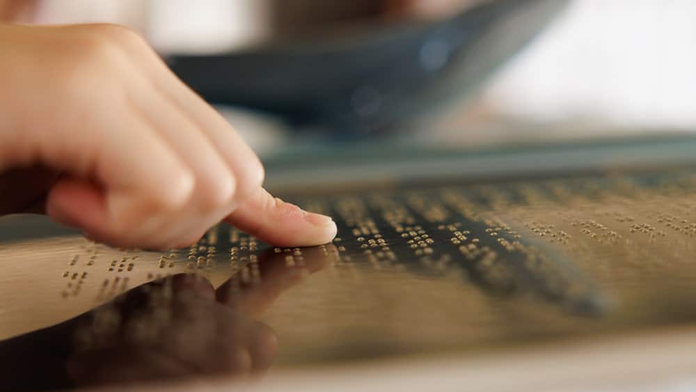 Dedo leyendo un rótulo con información en braille, realizado con impresión digital.